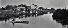 Holiday crowd by fenland River,  with man fishing in punt near public house
