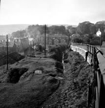 Penydarren Tramroad (Castle Morlais Line).  Pen Yard, Pen-y-Darren. The Tramroad cutting below and parallel to the High Street. View looking west showing the old tramroad cutting between the telegraph pole and the roadway retaining wall. 24th October 1949  (1)